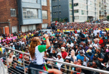 A woman addresses a large crowd gathered in an urban area in South Africa