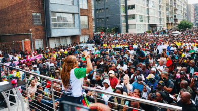 A woman addresses a large crowd gathered in an urban area in South Africa