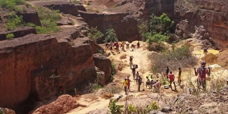A group of people walking and working through a rugged, dry rocky landscape surrounded by steep reddish-brown cliffs and eroded earth.