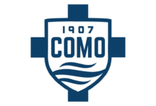 Logo of Como 1907, featuring a blue-and-white shield with the text “1907 COMO” and stylized wave lines representing Lake Como.